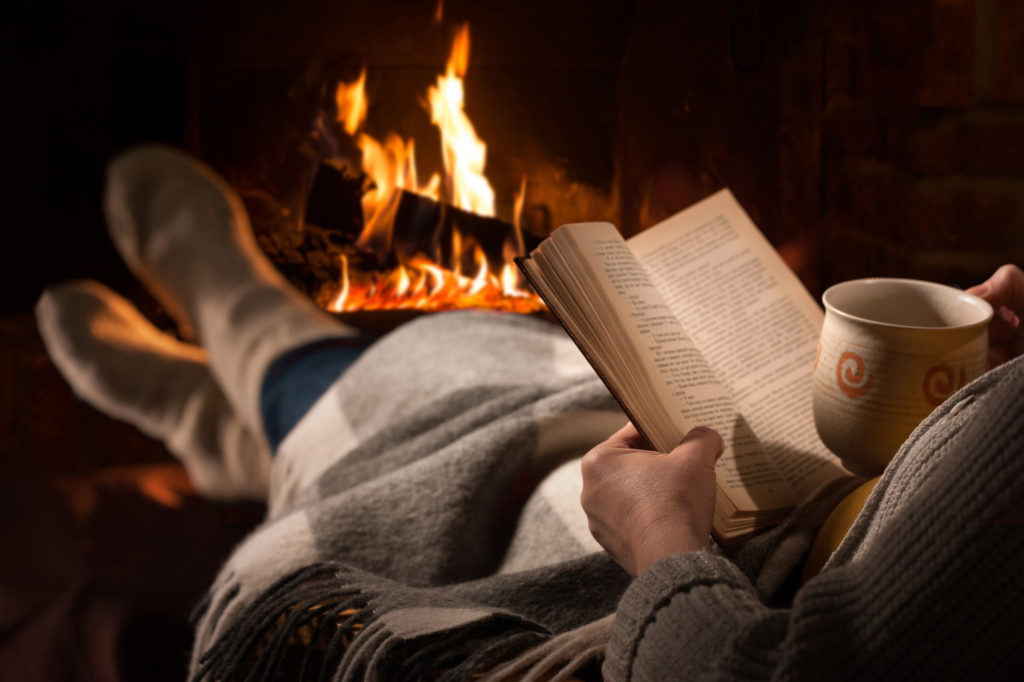 woman sitting by fireplace with a book
