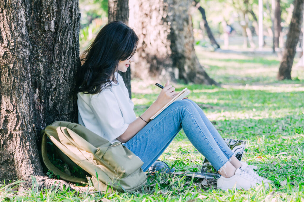 woman sitting by a tree journaling
